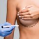 Cropped view of doctor in latex glove holding marker near naked woman with marks on breast isolated